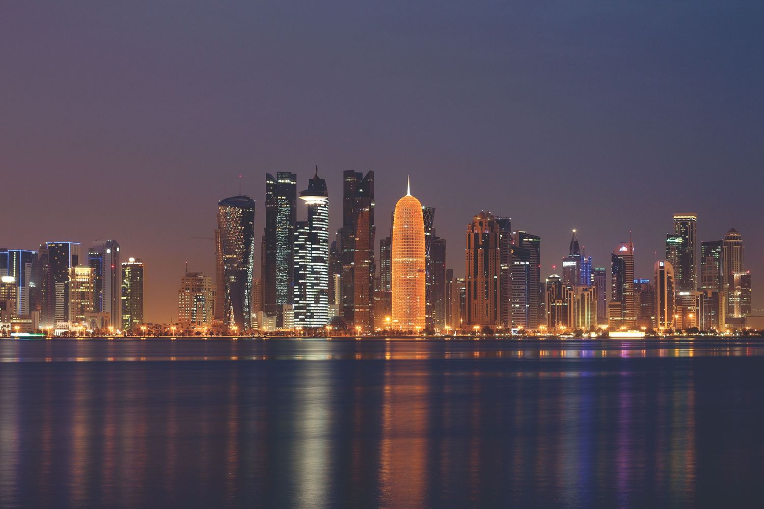 The Doha skyline lit at dusk and reflected in the bay