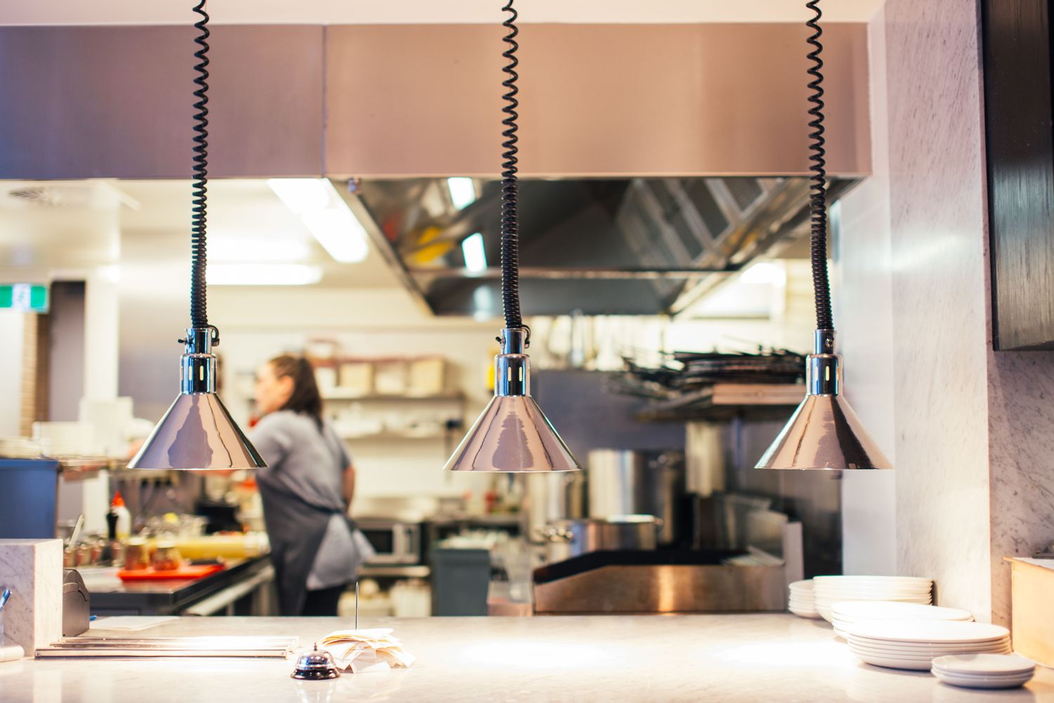A commercial kitchen pass with heat lamps and a cook preparing food behind it