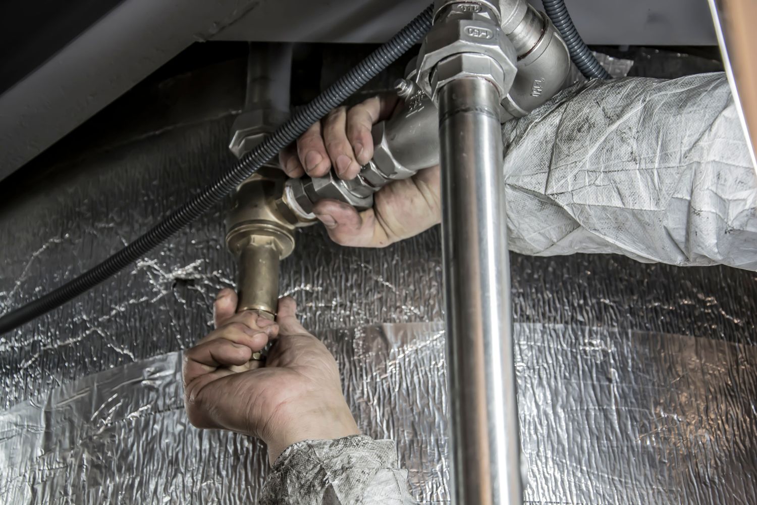 A plumber connecting brass and steel pipes under insulation